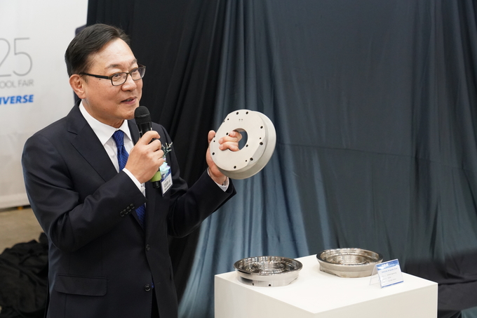 DIMF2025 DLX 언베일행사에서 김원종 대표이사가 적층제조로 제작된 부품을 들어보이고 있다.